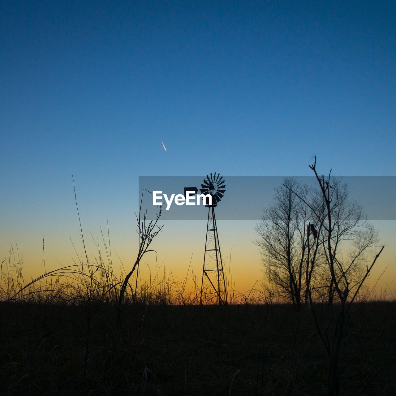 Silhouette of windmill on field against clear sky during sunset