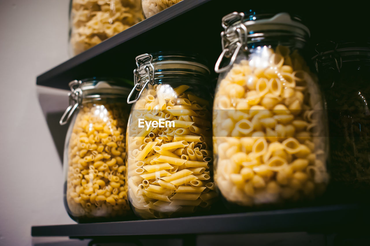 Close-up of pasta in jars on shelf in kitchen at home