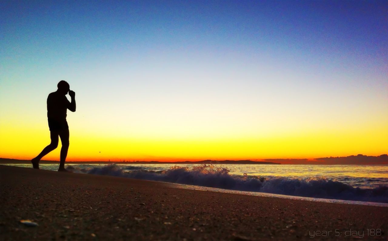 Silhouette man walking towards sea on beach at sunset