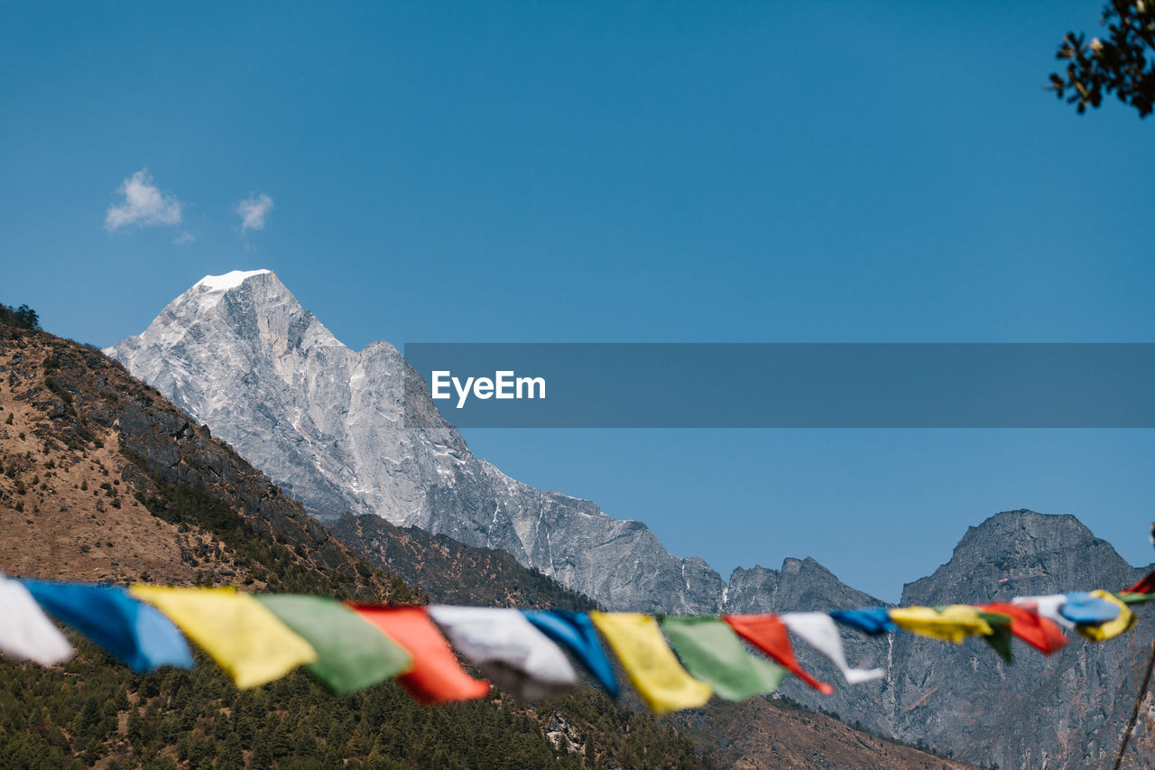 Traditional colorful prayer flags hanging on rope against rocky mountains and blue sky in sunny day