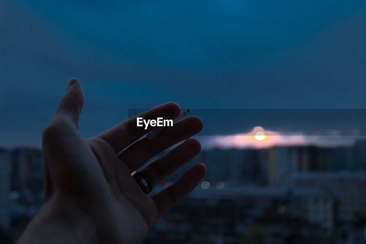 Close-up of hand holding cigarette against sky at night