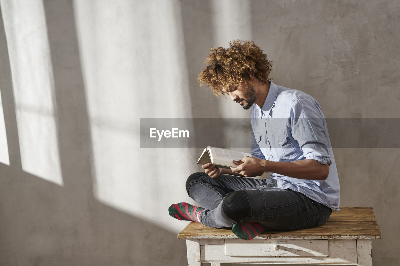 Young man sitting on wooden table reading book