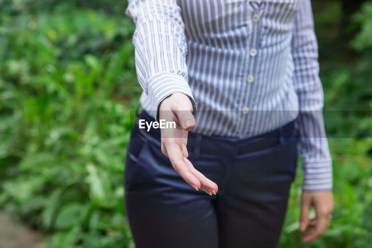 Midsection of businesswoman giving handshake while standing against plants at park