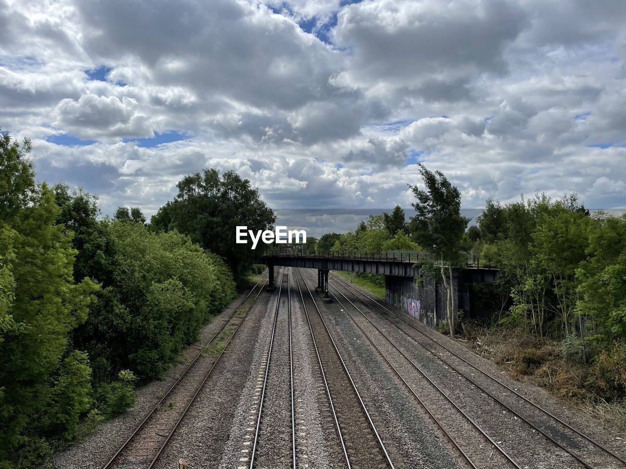 rail transportation, railroad track, track, tree, cloud, plant, transport, sky, transportation, nature, railway, no people, the way forward, mode of transportation, public transportation, vehicle, travel, vanishing point, outdoors, day, diminishing perspective, rolling stock, train, environment, architecture, growth