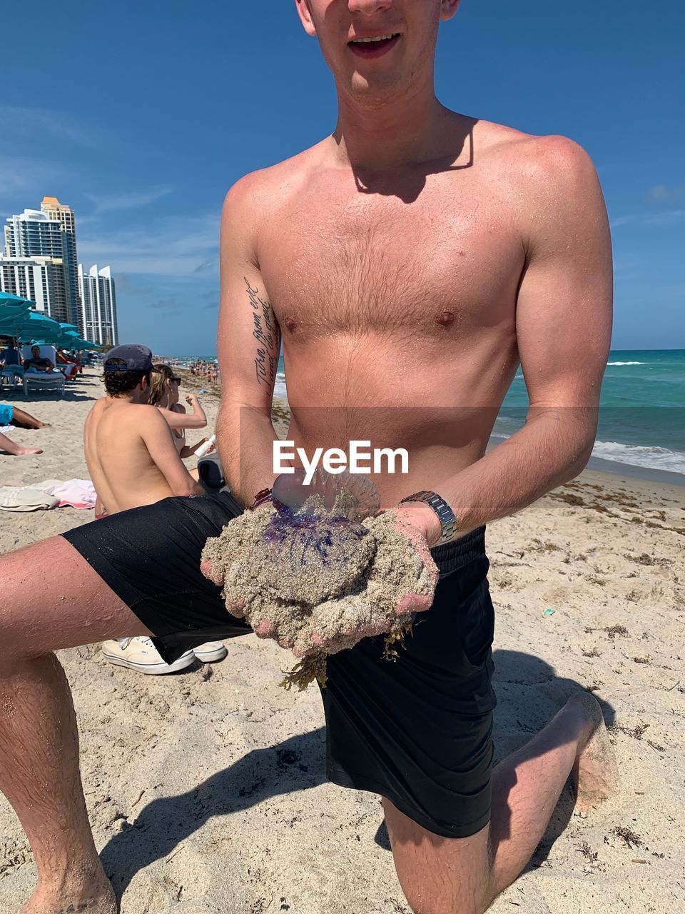 FULL LENGTH OF SHIRTLESS MAN HOLDING SUNGLASSES AGAINST SKY