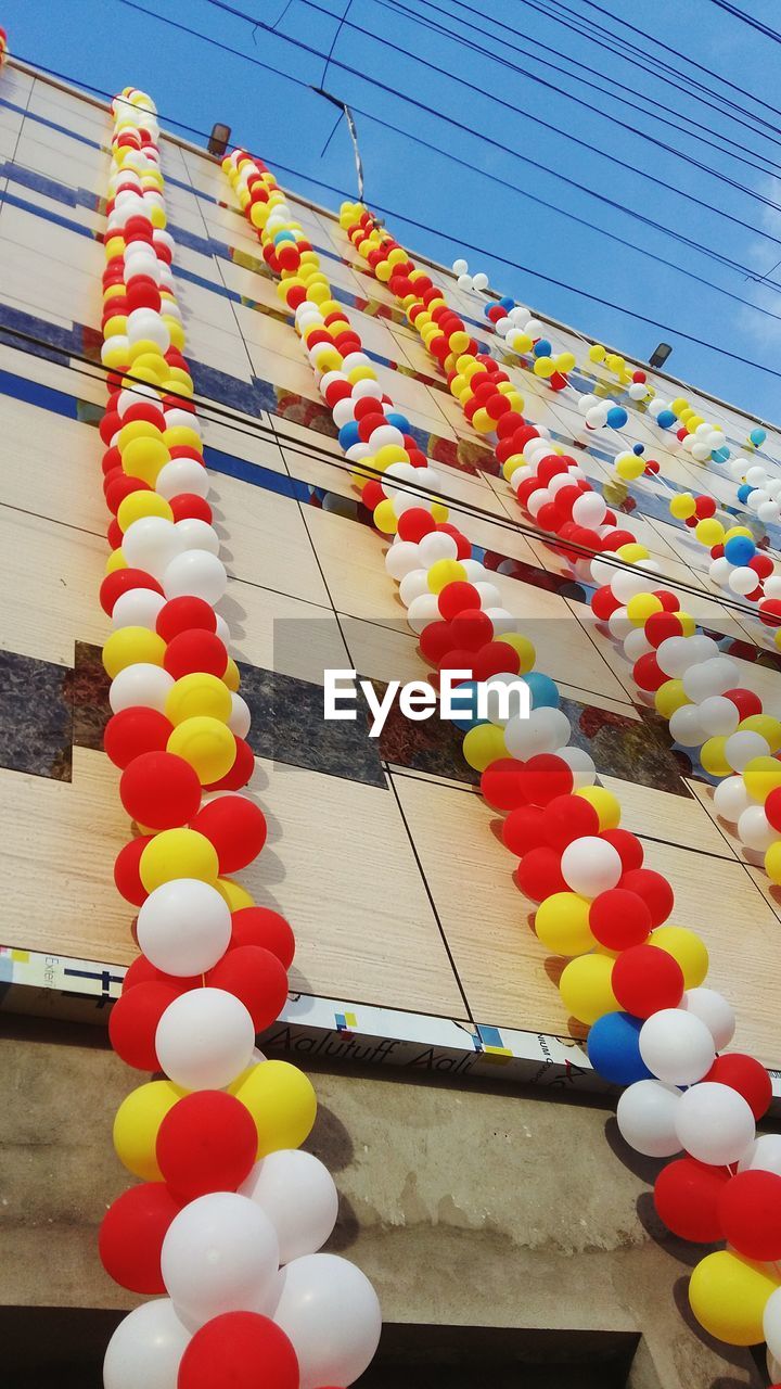 LOW ANGLE VIEW OF MULTI COLORED BALLOONS IN ROW AGAINST SKY