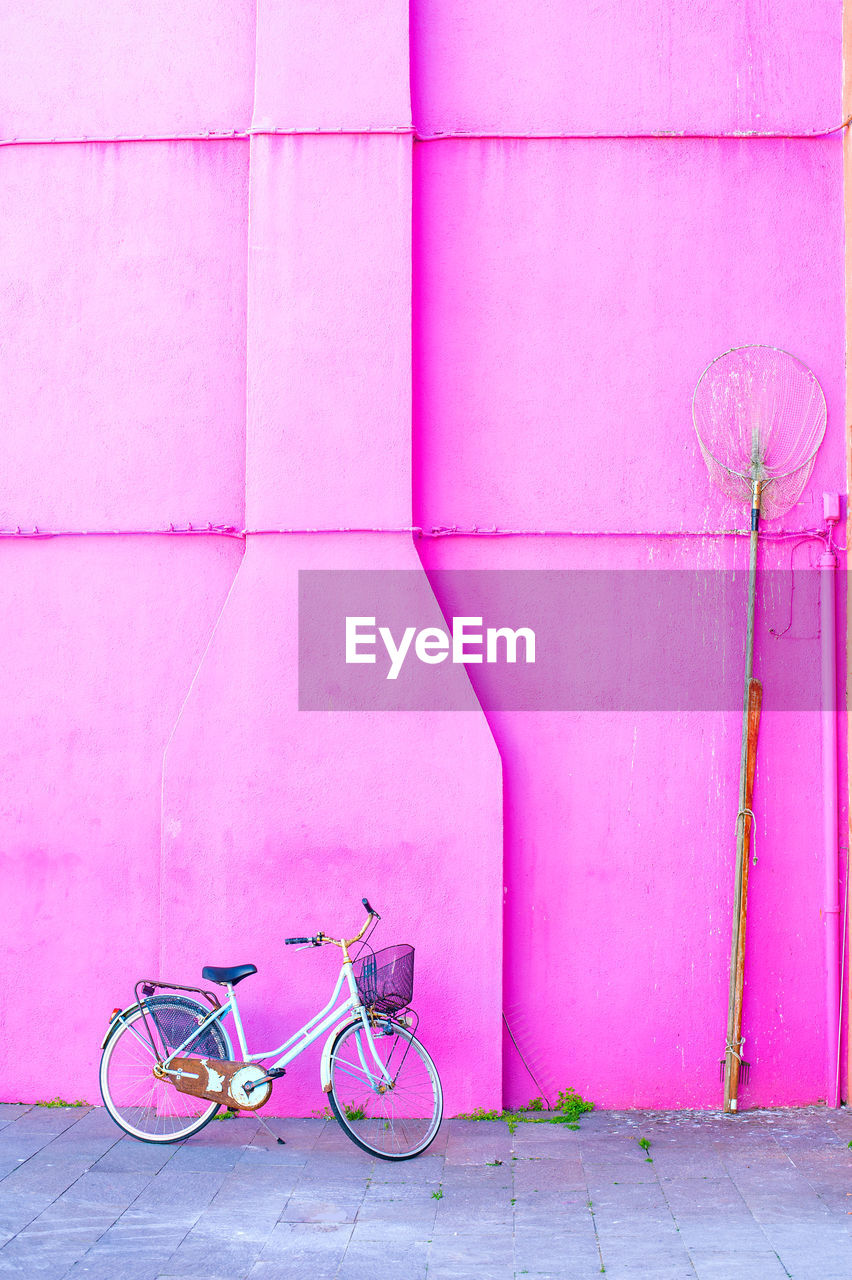 BICYCLE LEANING ON WALL BY SIDEWALK