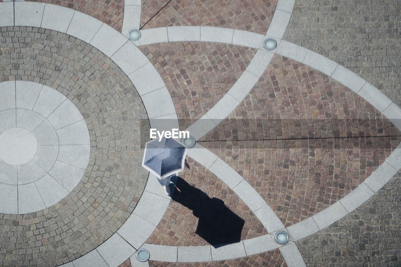 Aerial view of geometrical flooring and a pedestrian with an umbrella in hand in a sunny day