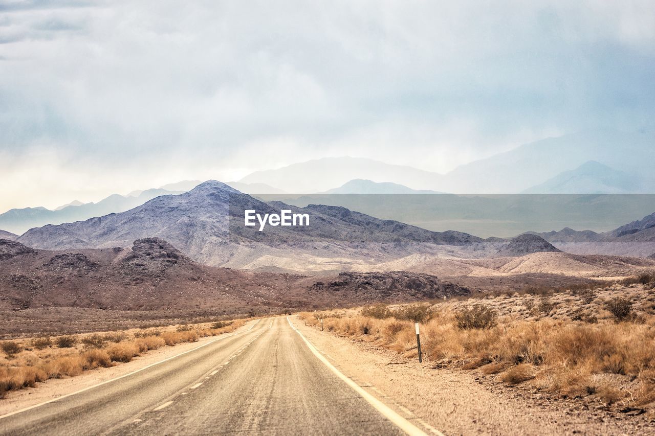 Empty road leading towards mountains against sky