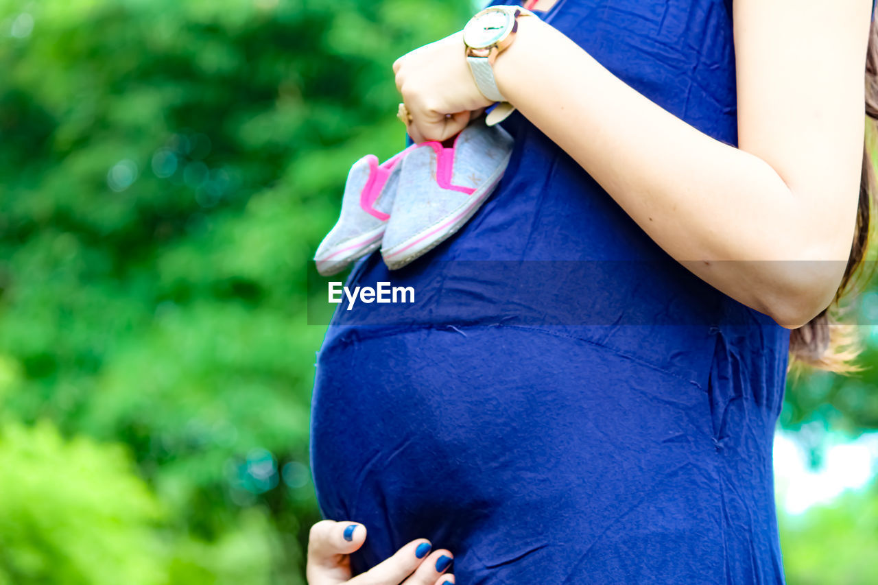 Midsection of pregnant woman holding baby booties while standing outdoors