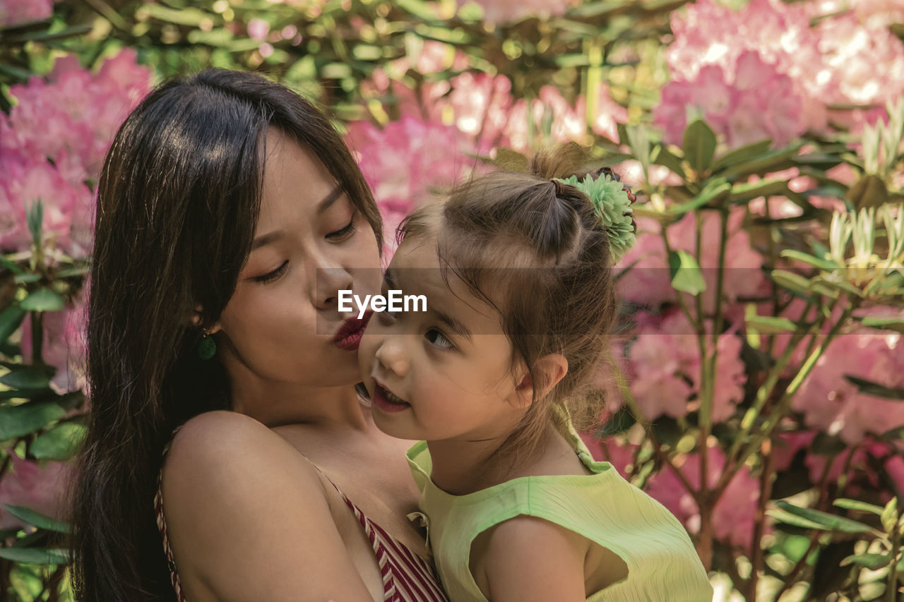 Woman kissing daughter while standing by plants