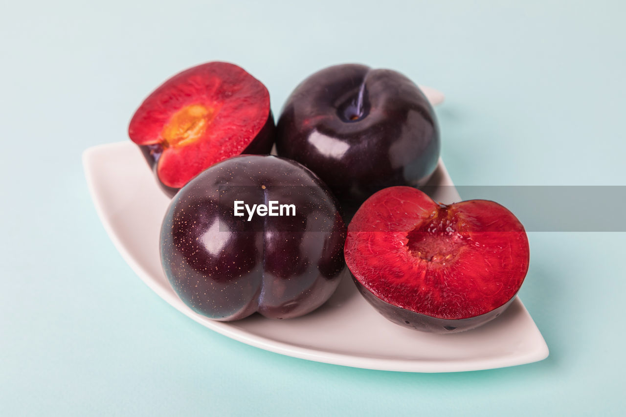 On a white saucer is a large plum, cut in half, and next to it is a whole plum.