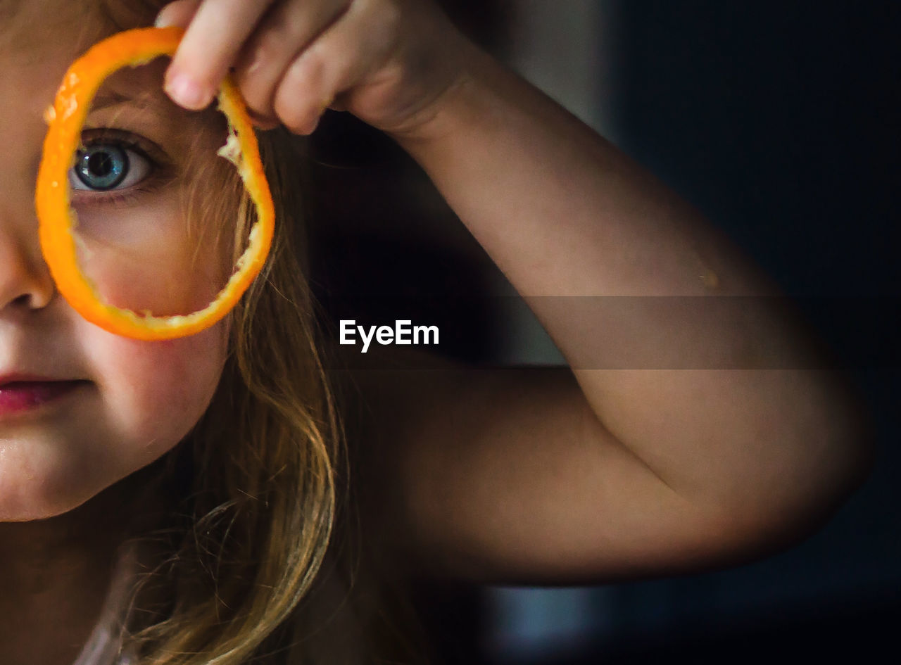 Close-up portrait of young girl looking through orange peel