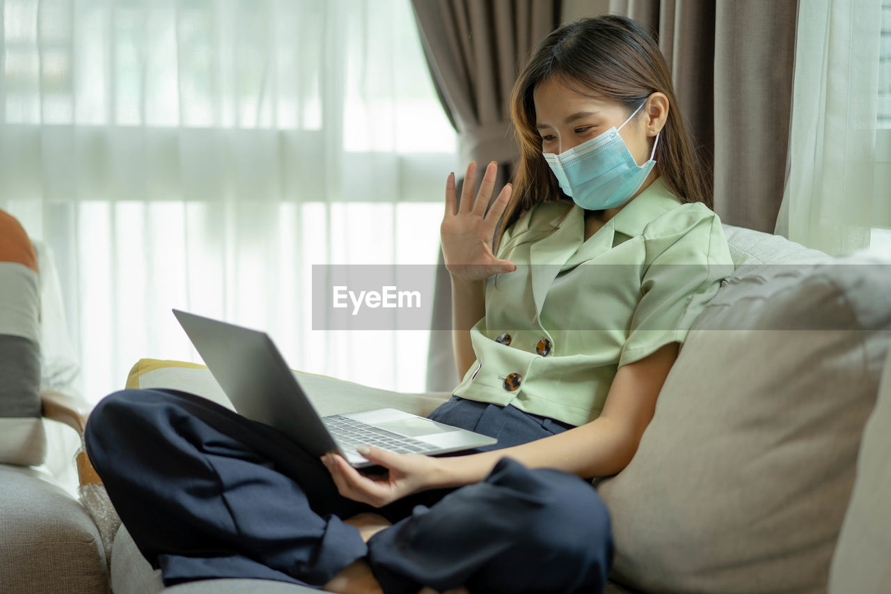 Young woman wearing mask talking on video call at home