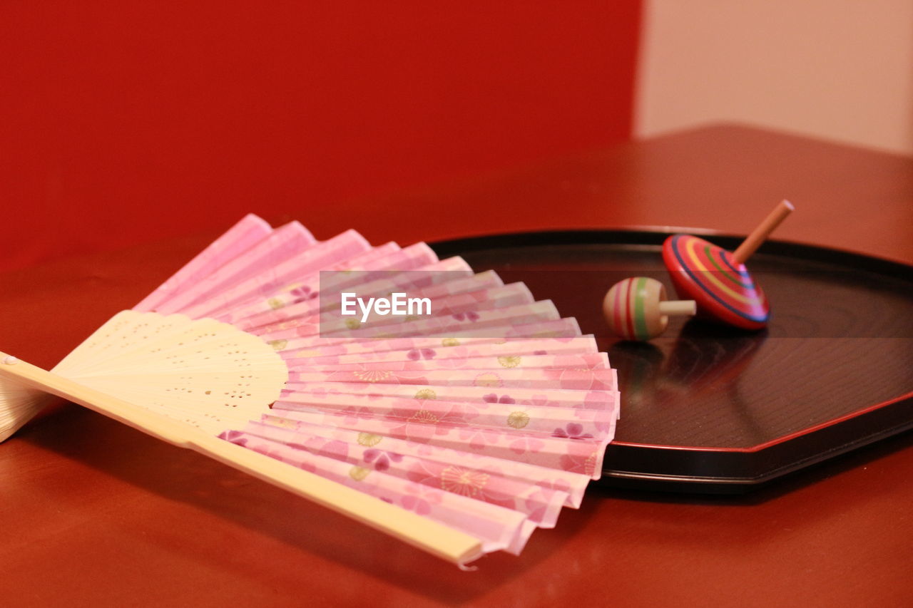 Close-up of pink folding fan with spinning tops on table