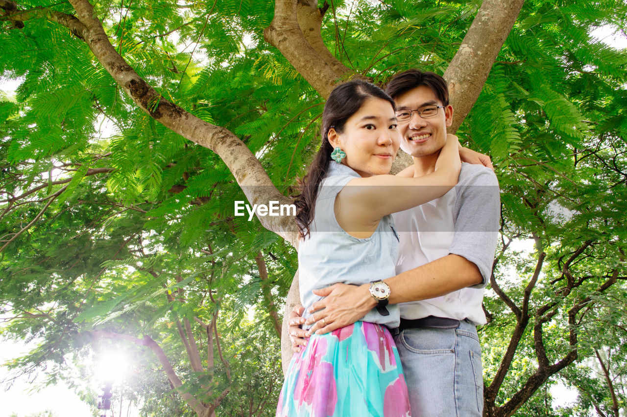 Portrait of young woman standing against tree