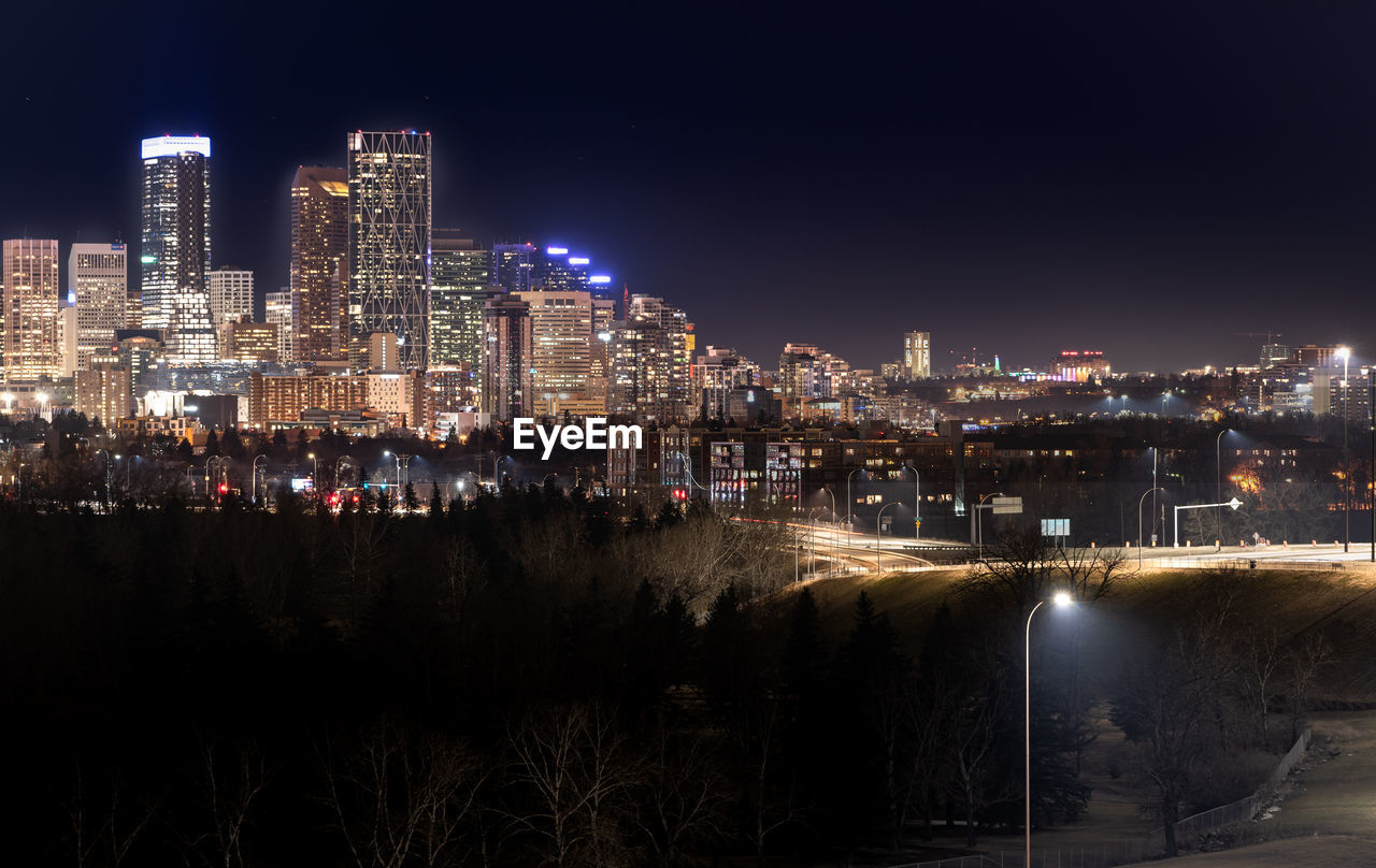 HIGH ANGLE VIEW OF ILLUMINATED BUILDINGS BY RIVER AGAINST SKY