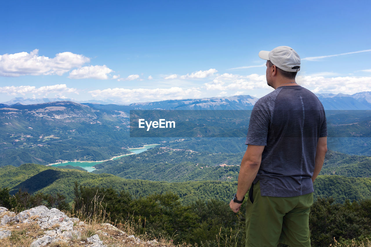 REAR VIEW OF MAN STANDING ON MOUNTAIN