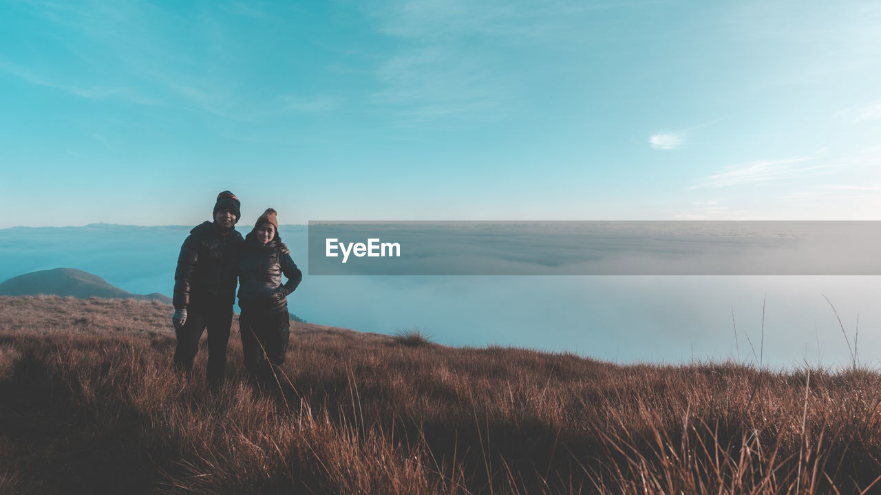 Couple standing on cliff against cloudy sky