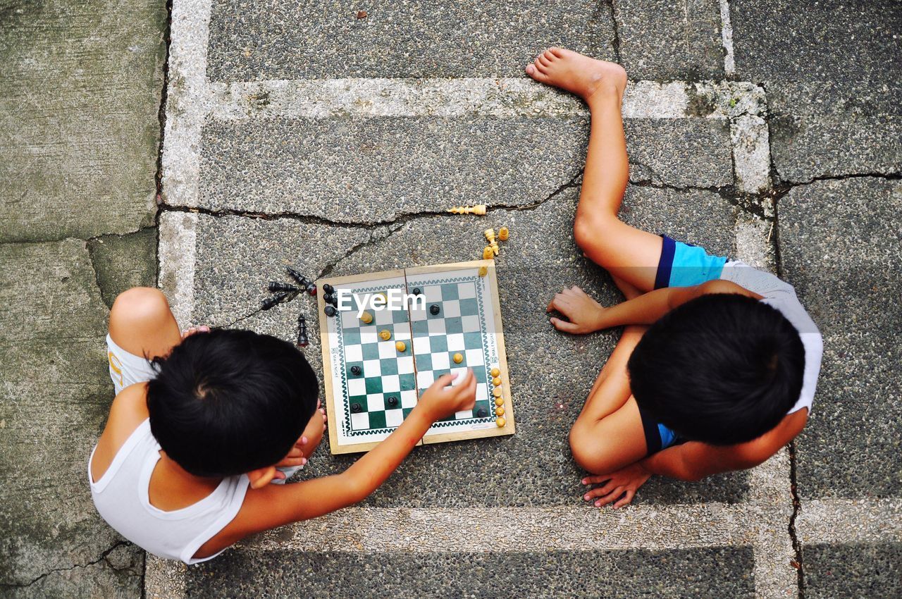 High angle view of friends playing chess while sitting on footpath