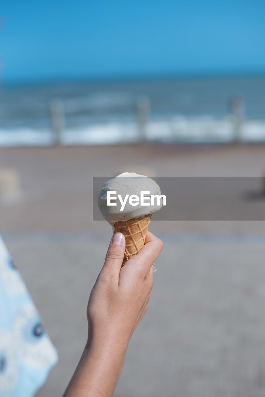 Cropped hand holding ice cream cone at beach