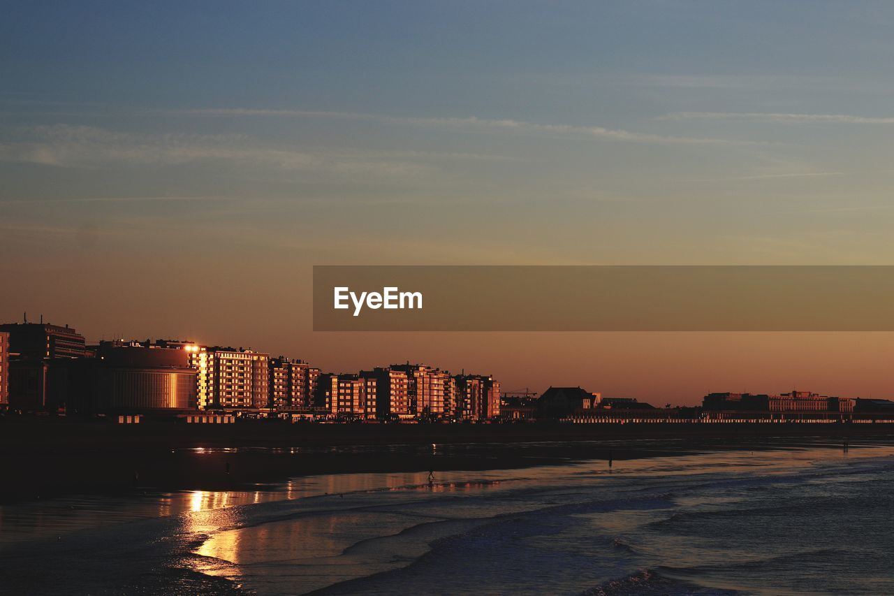 Buildings by sea against sky at sunset