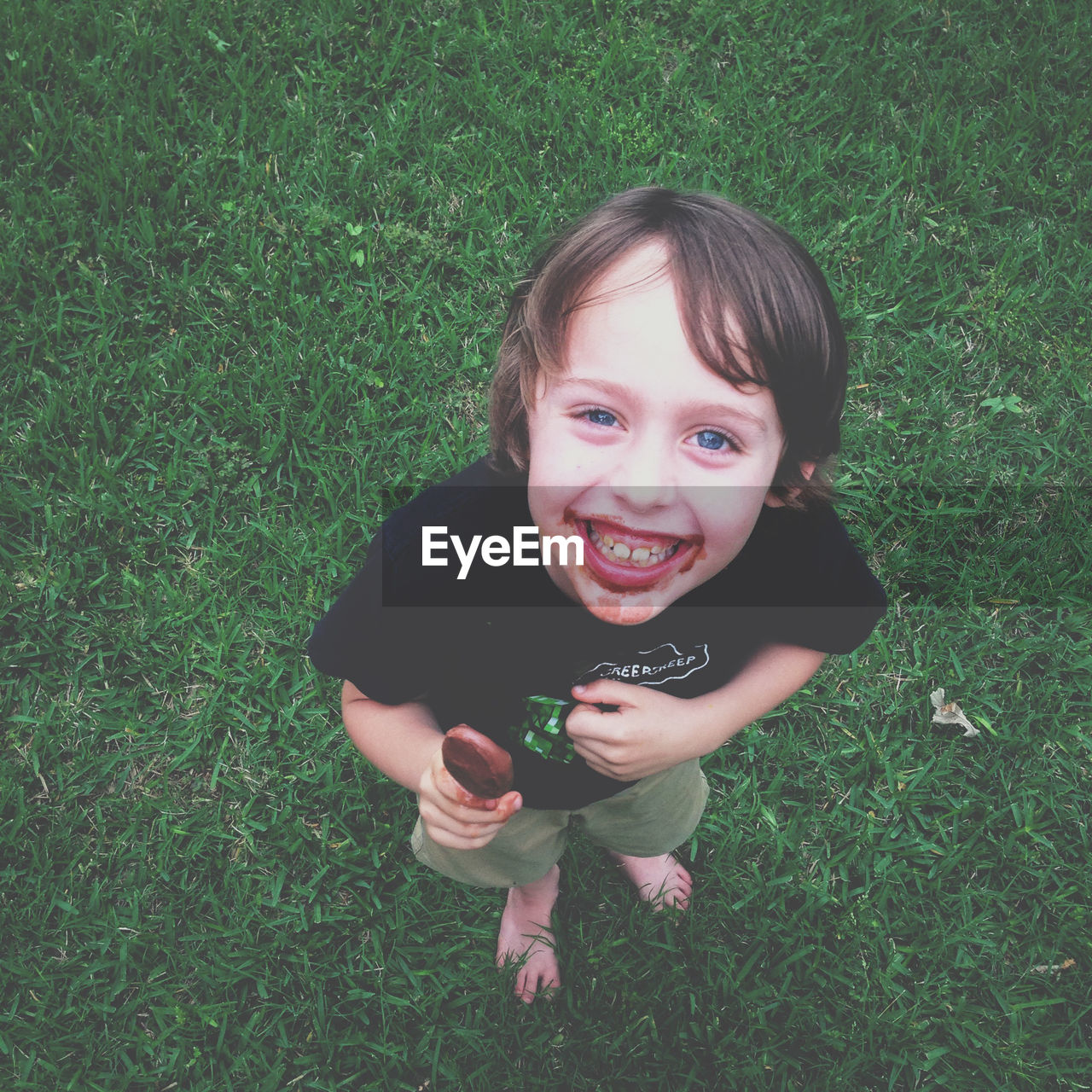 High angle portrait of happy boy eating ice cream on grassy field