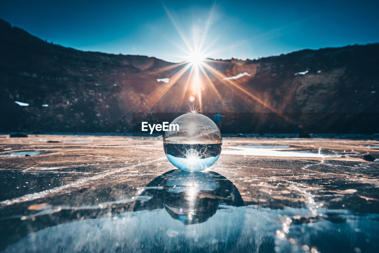 Crystal ball on field against mountain during sunny day