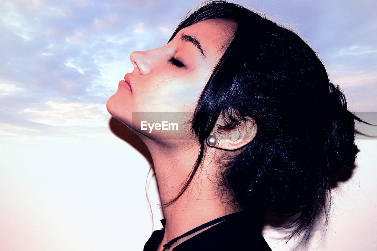 Side view close-up of young woman with closed eyes against sky