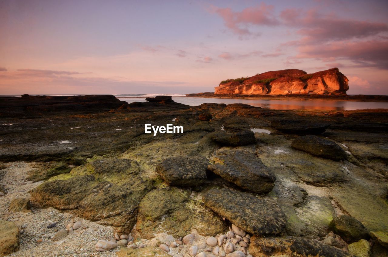 Rocks on shore against sky during sunset