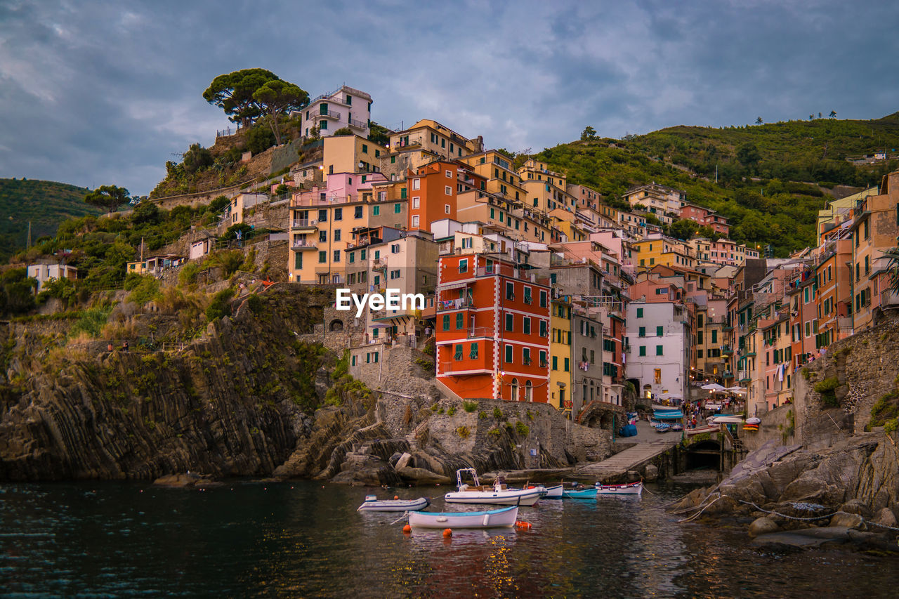 SAILBOATS MOORED ON RIVER AMIDST BUILDINGS AGAINST SKY