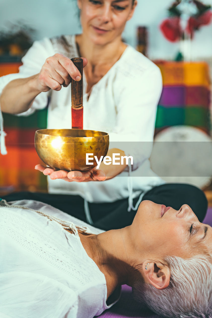 Midsection of woman playing singing bowl for customer in spa