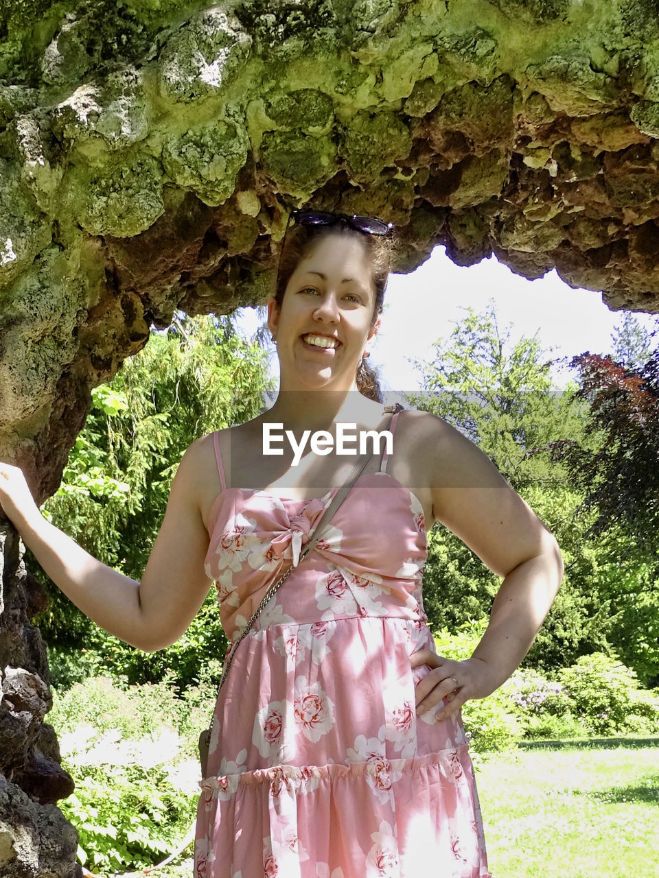 PORTRAIT OF A SMILING YOUNG WOMAN STANDING AGAINST TREES