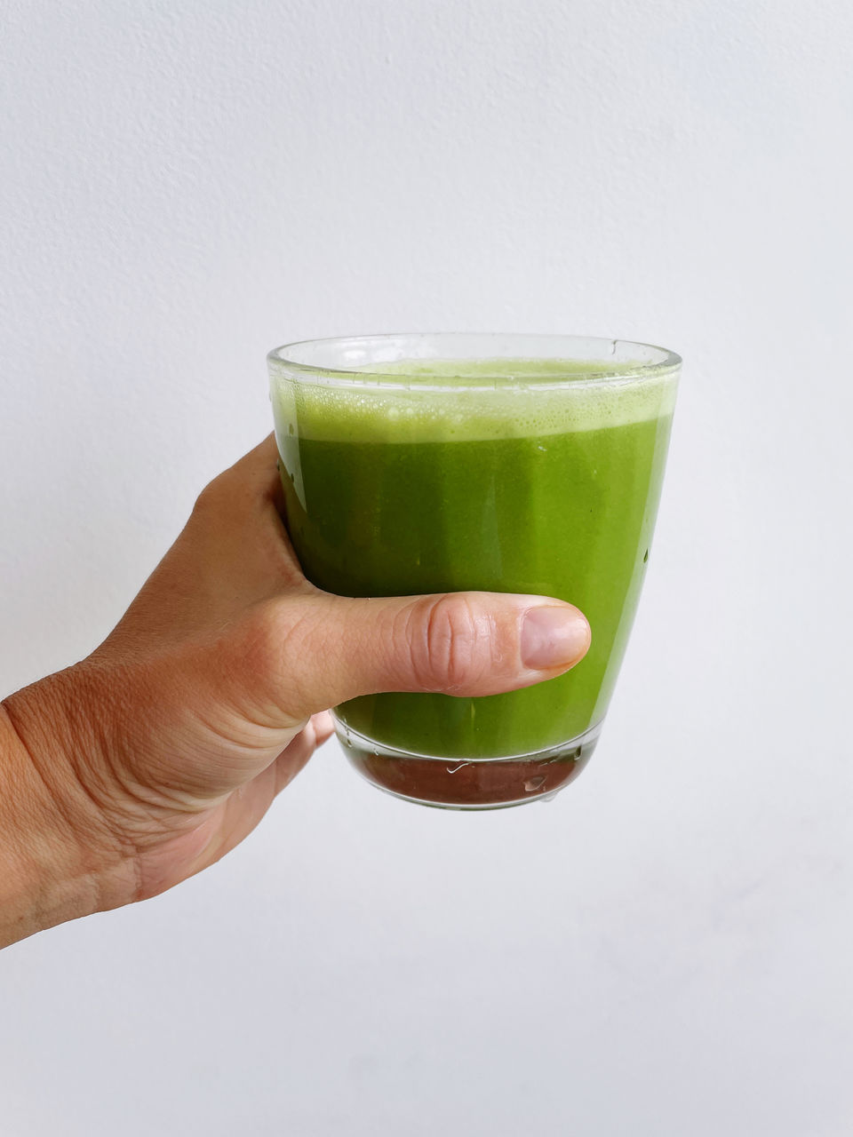 Hand holding green juice against white wall