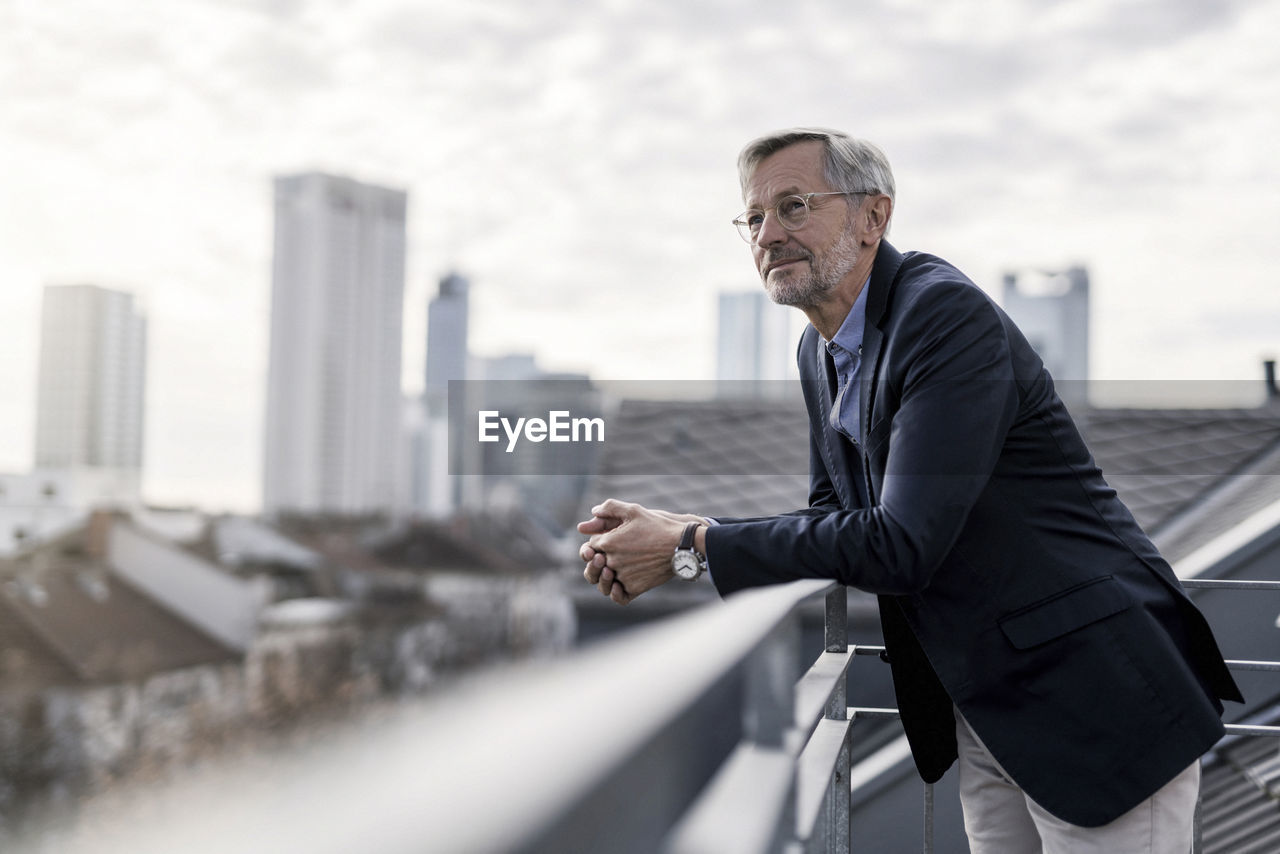 Grey-haired businessman standing on balcony looking over city