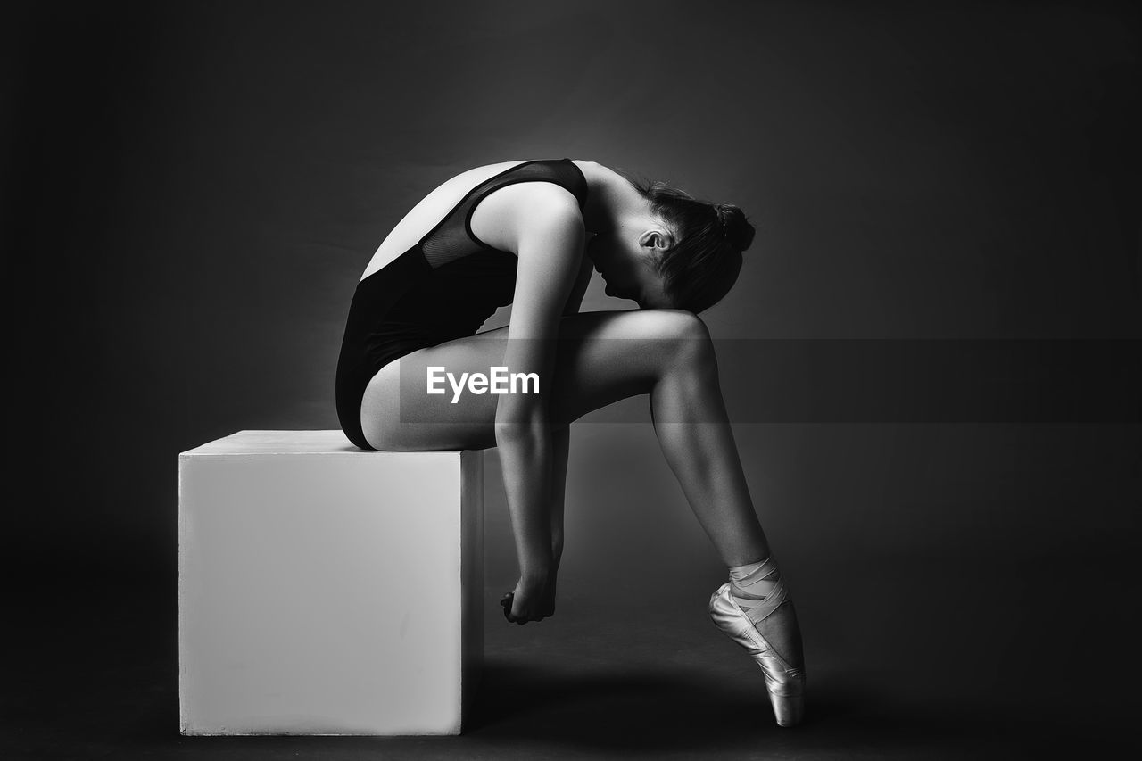 Side view ballet dancer sitting on box against gray background
