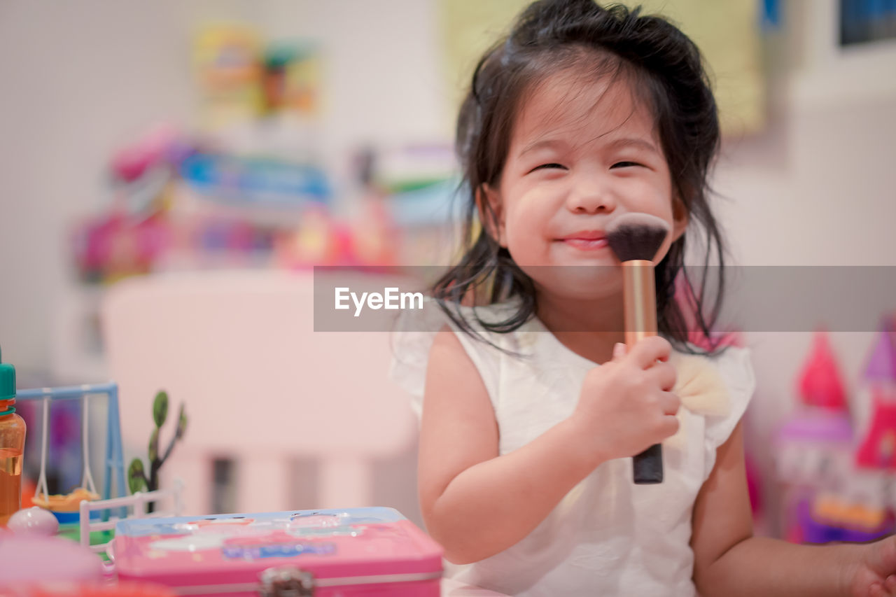 Portrait of smiling cute girl holding make-up brush at home