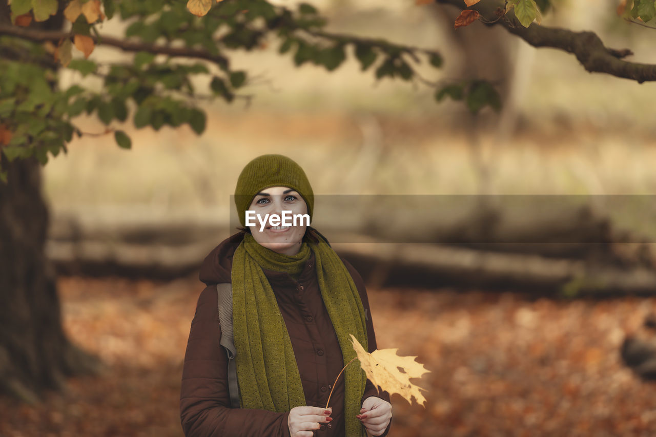 Portrait of smiling woman holding autumn leaf standing at park