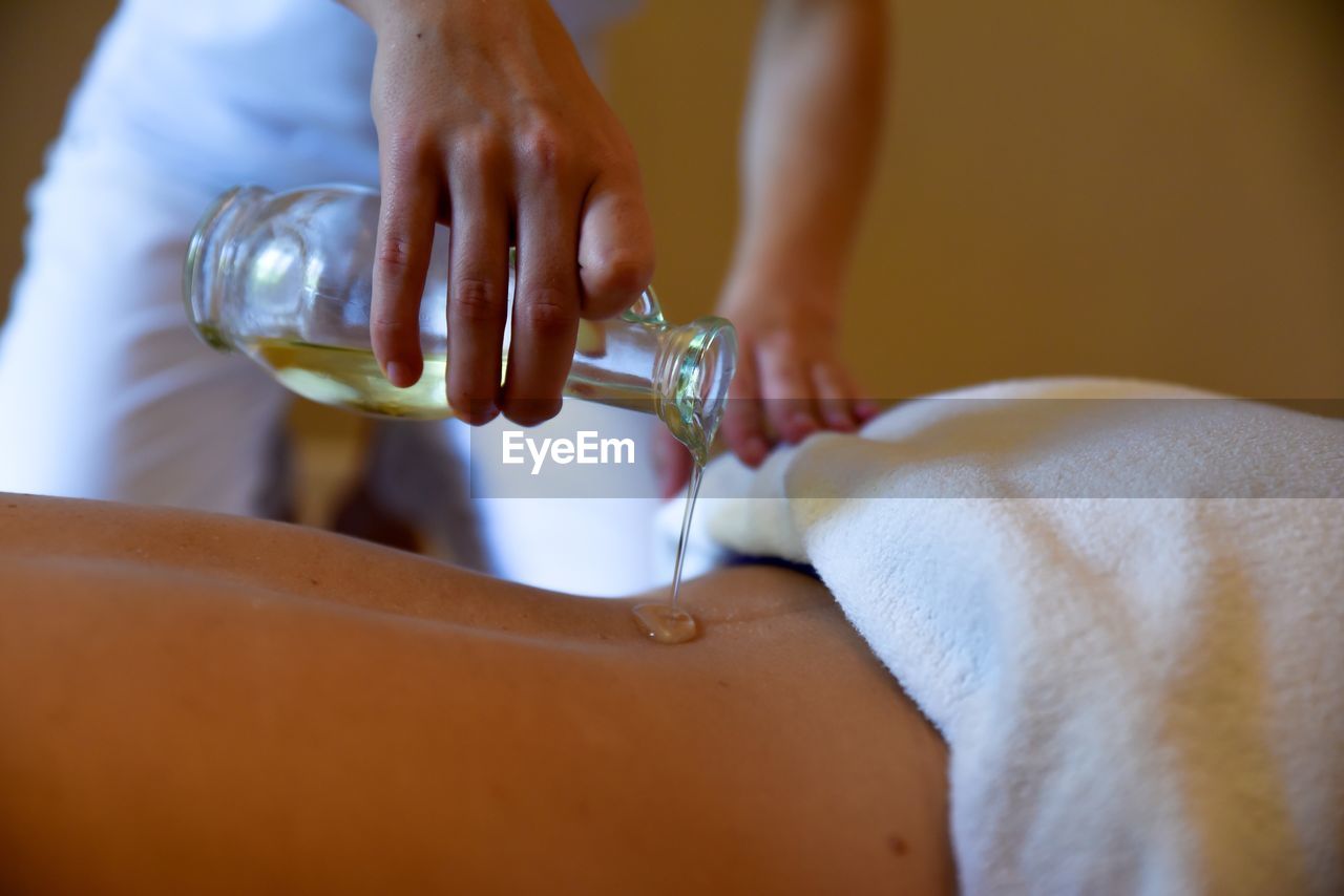 Midsection of woman pouring essential oil on customer back at spa