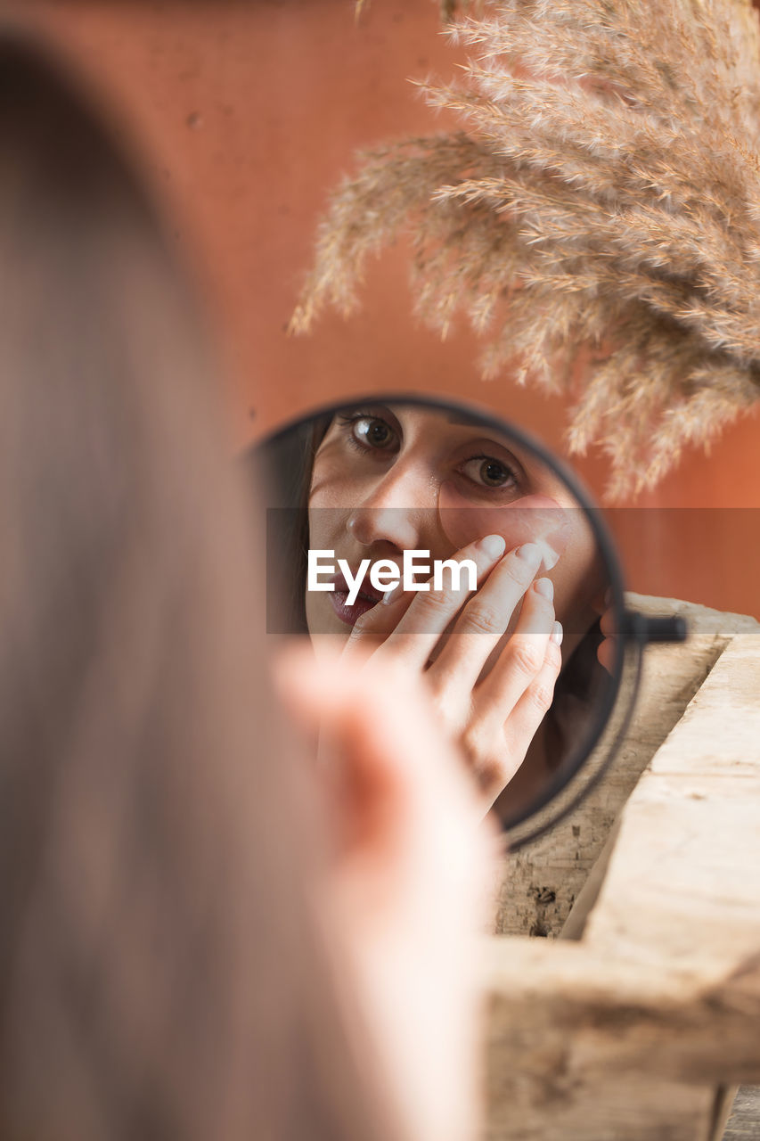 Mirror reflection of woman applying under-eye patch at dressing table closeup