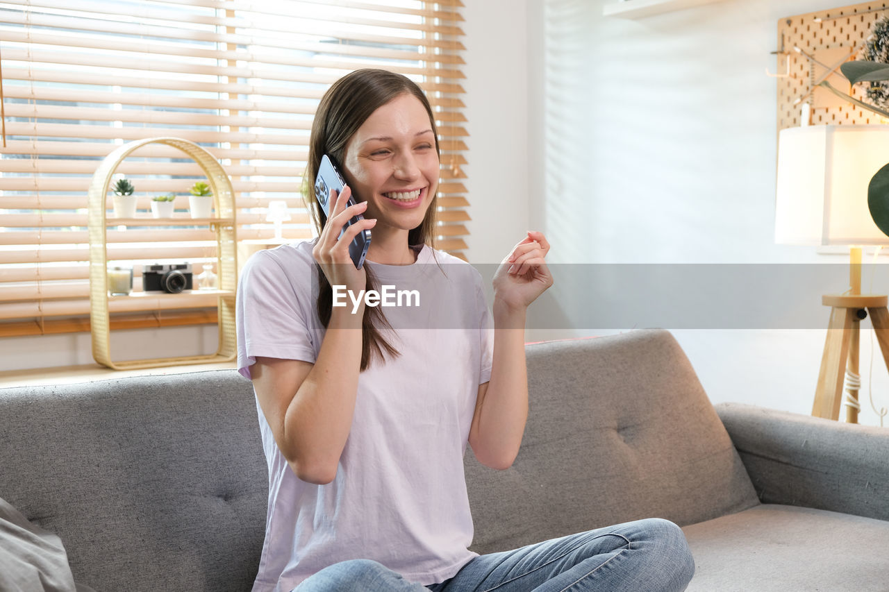 portrait of young woman using phone while sitting on sofa at home