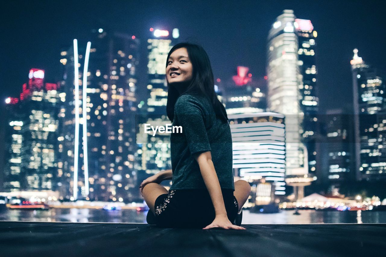 Rear view of happy young woman against illuminated cityscape