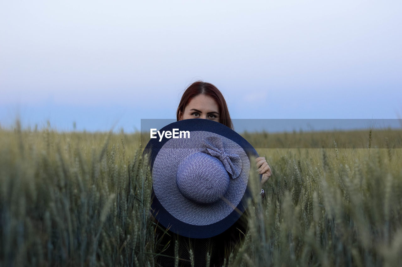 PORTRAIT OF BEAUTIFUL WOMAN STANDING IN FARM AGAINST CLEAR SKY