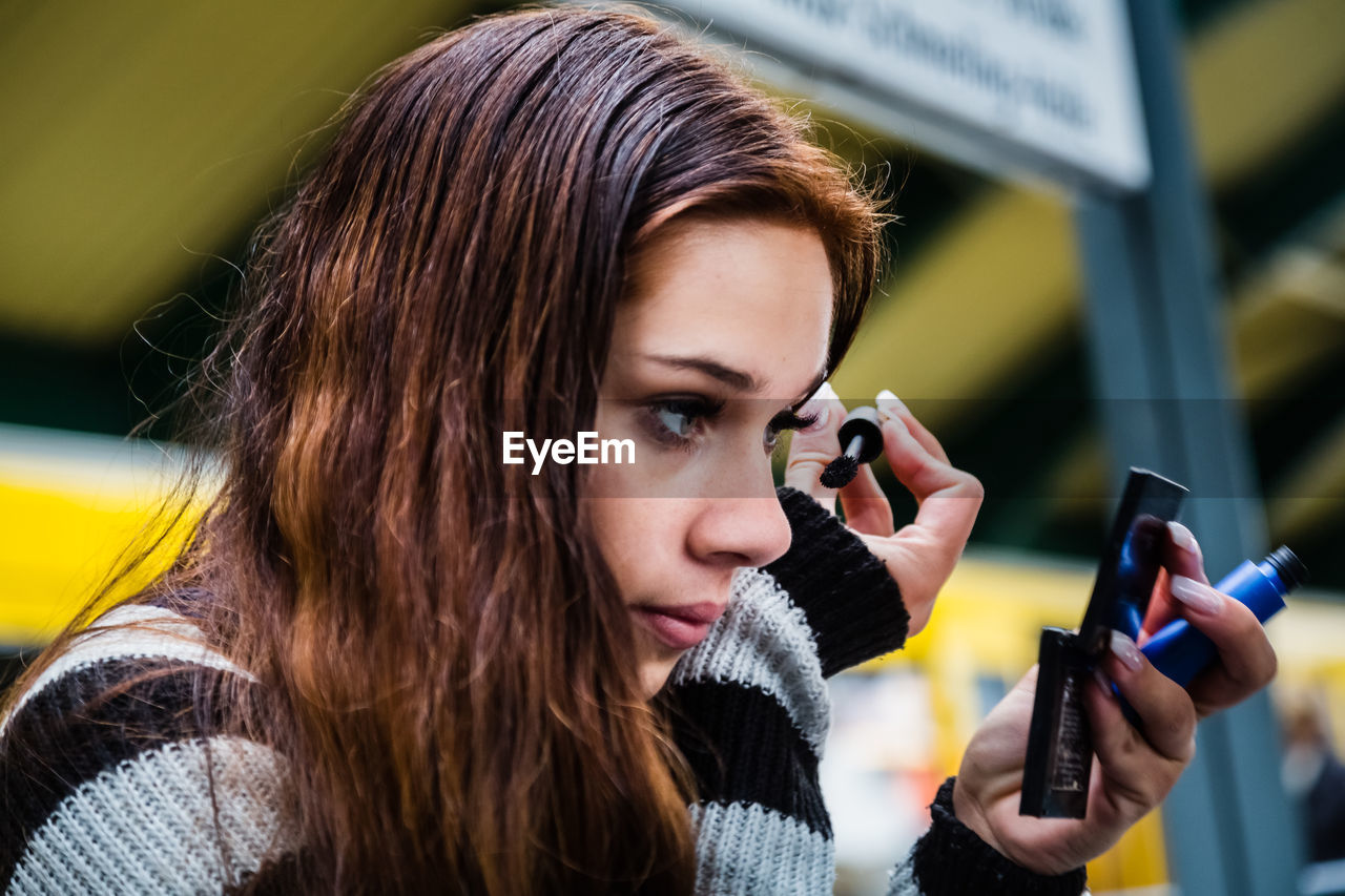 Close-up of woman applying mascara while sitting at railroad station