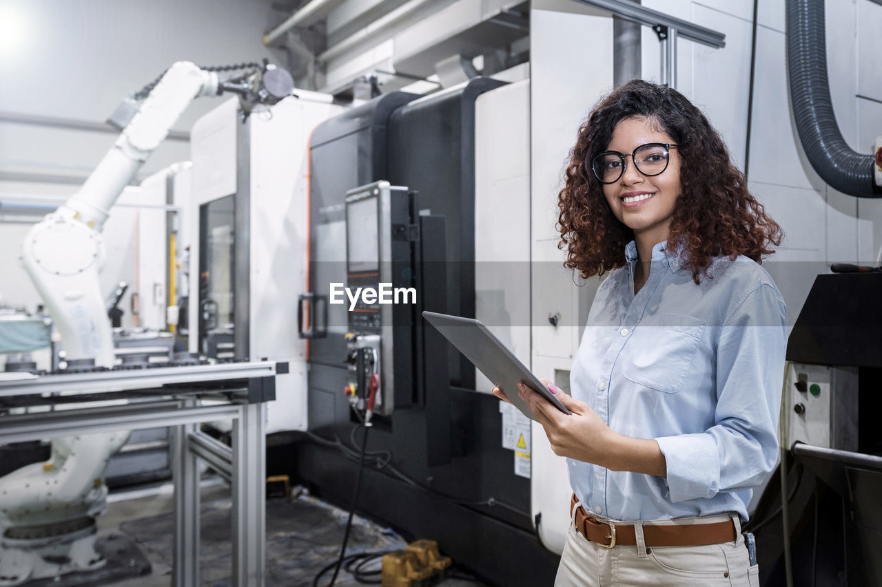 Happy engineer standing with tablet pc in front of machine