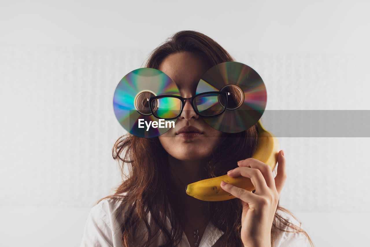 Woman wearing compact disc while holding banana