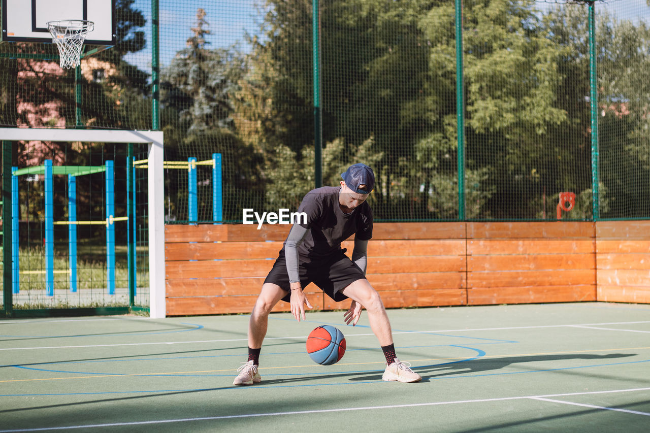 Boy practices dribbling basketball under his feet and improves his hand, body and foot coordination