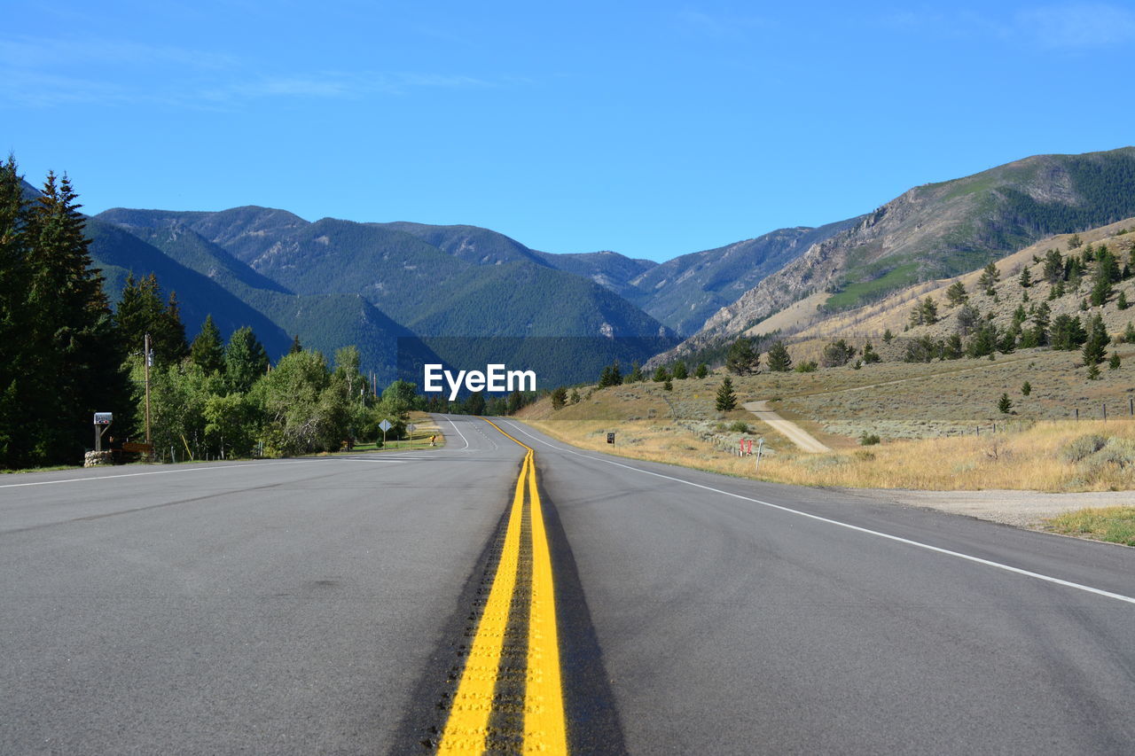 Empty road along mountains against clear blue sky