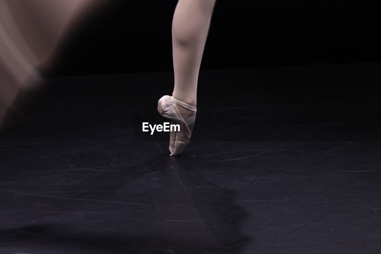 Low section of ballet dancer dancing against black background