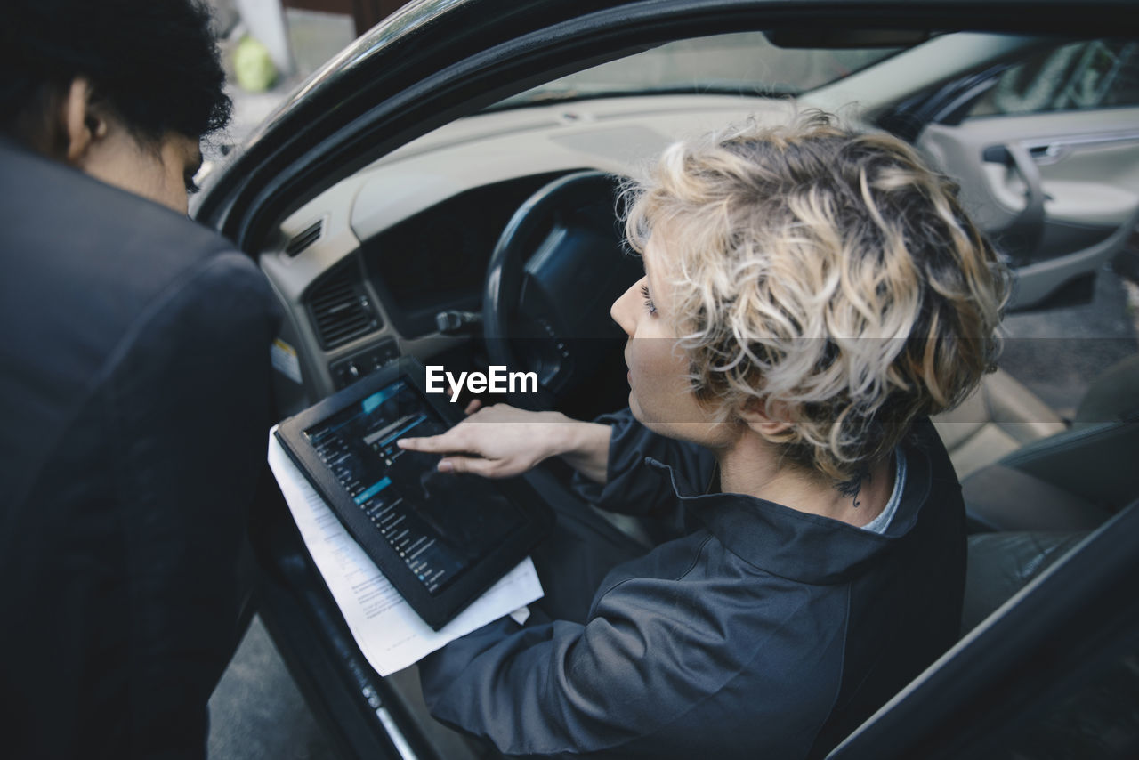 Female mechanic explaining customer over digital tablet while sitting in car